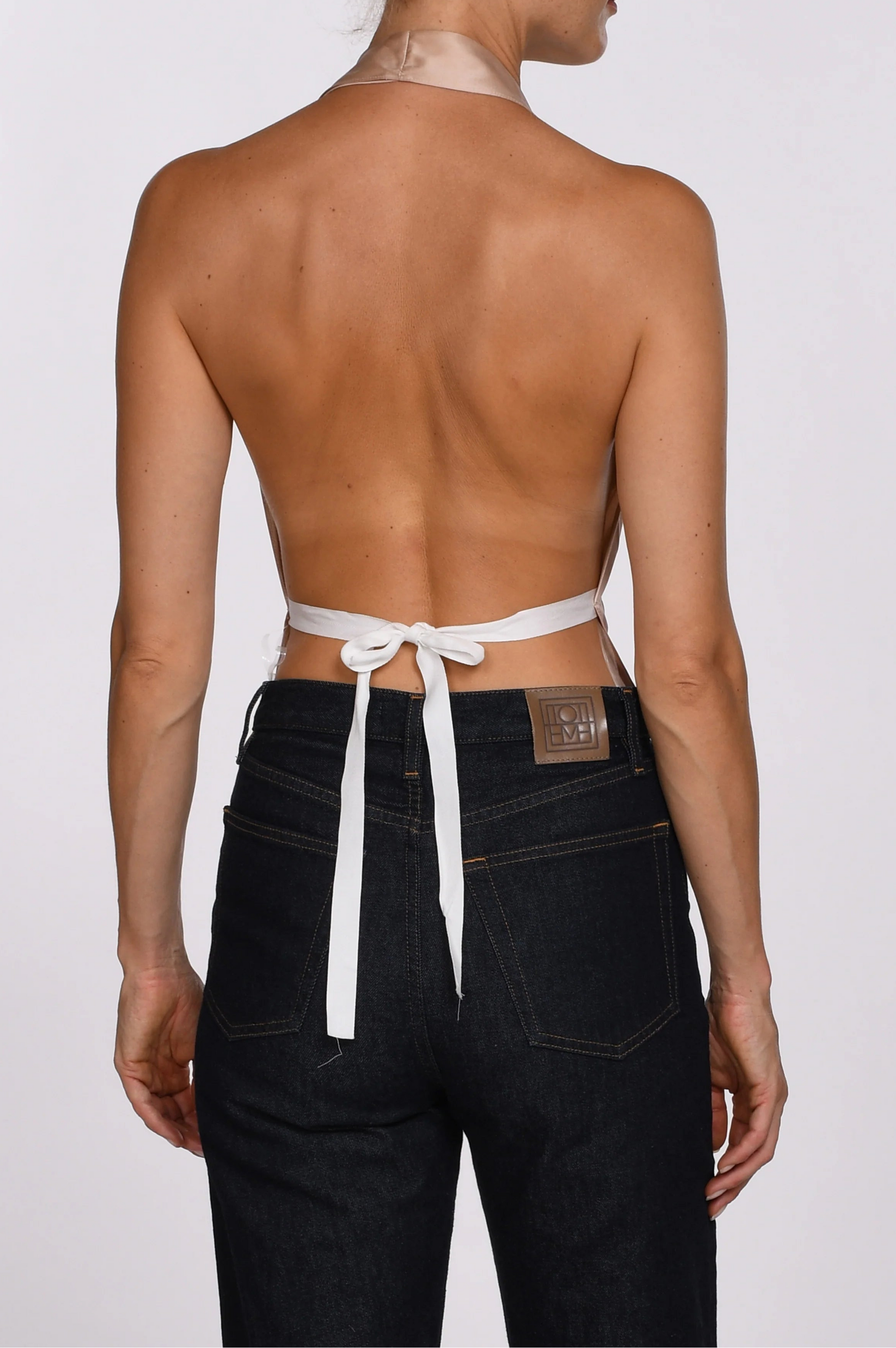 Woman wearing a strapless top with a white ribbon and black pants on a plain background