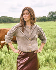 Woman wearing a textured sweater and leather skirt standing in a field with cows.