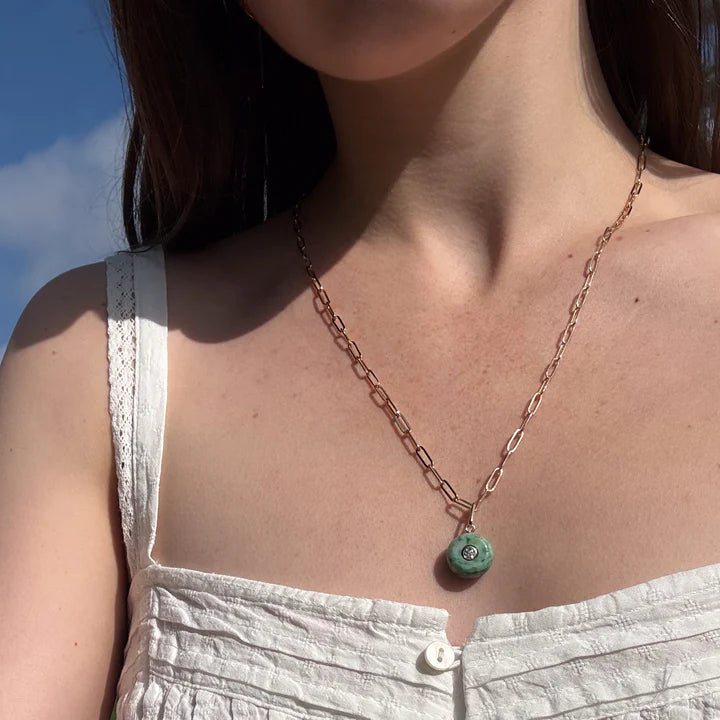 Necklace with a green pendant worn by a person against a blue sky.