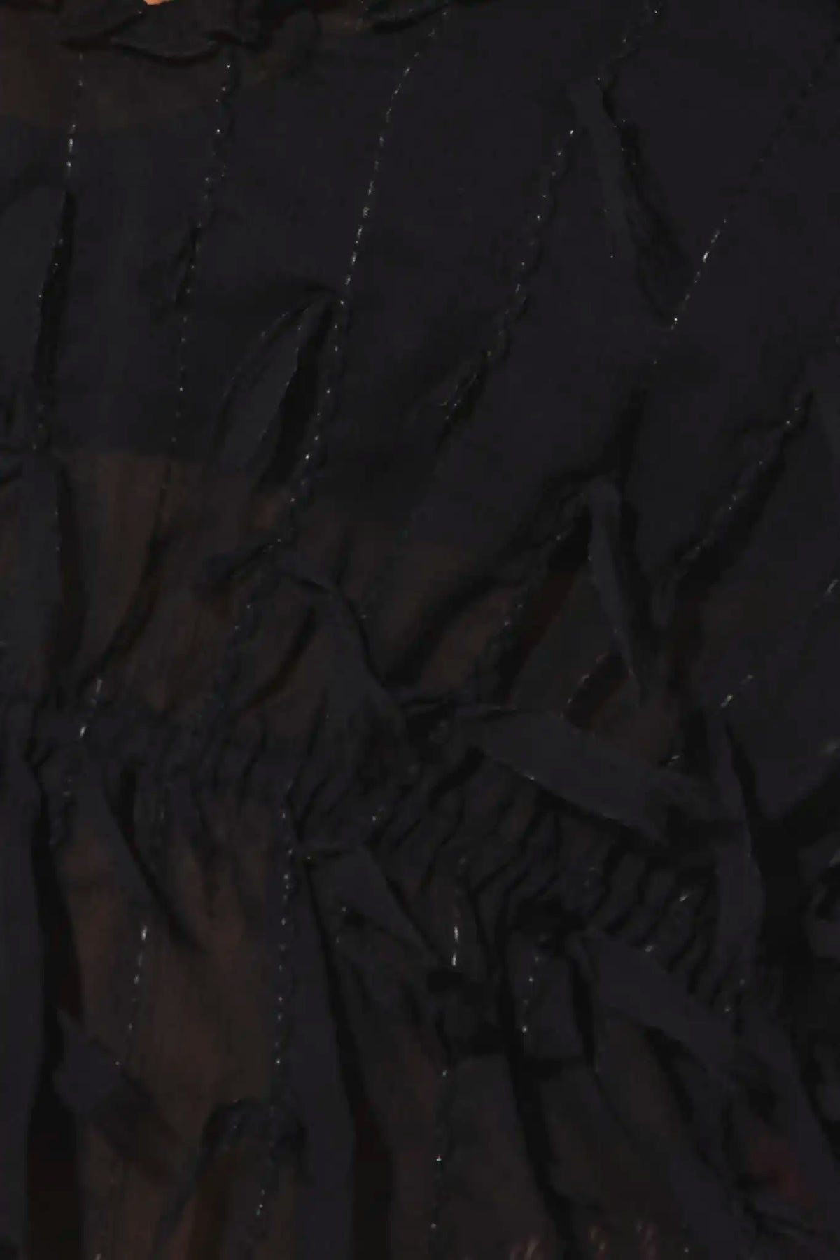Close-up of a black sheer mesh fabric with vertical ruching and small reflective embellishments.