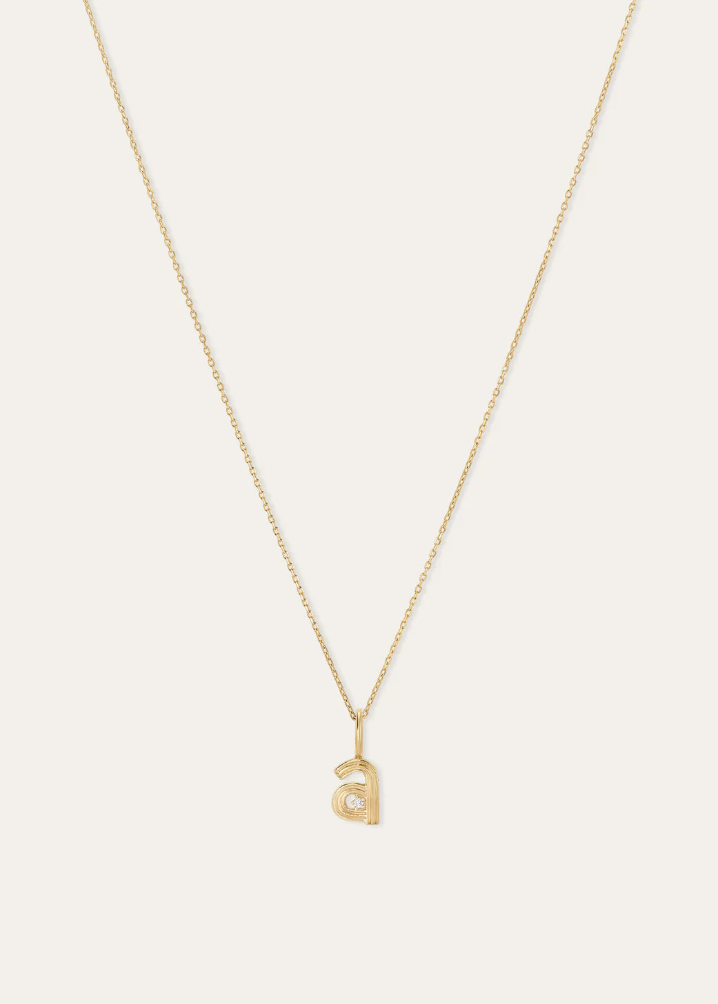A delicate gold chain necklace with a small lowercase letter 'a' pendant, displayed against a solid off-white background.