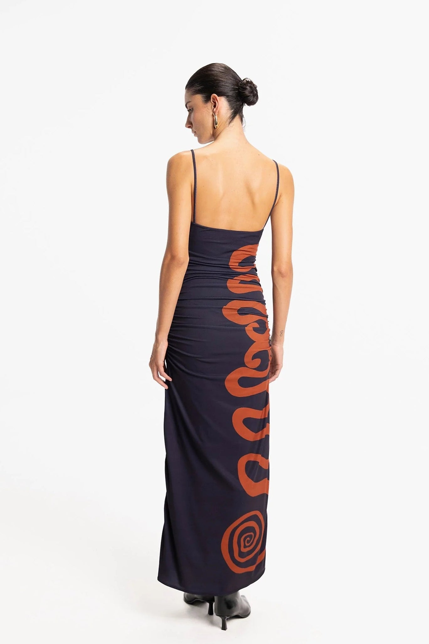 Woman wearing a long dress with orange patterns on a white background, back view