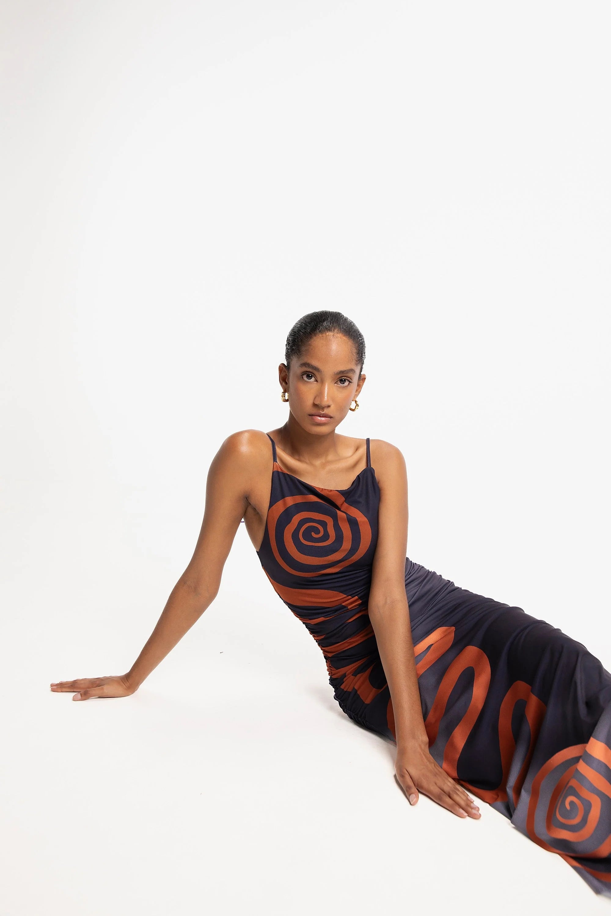 Woman sitting, wearing a dress with spiral pattern on a white background