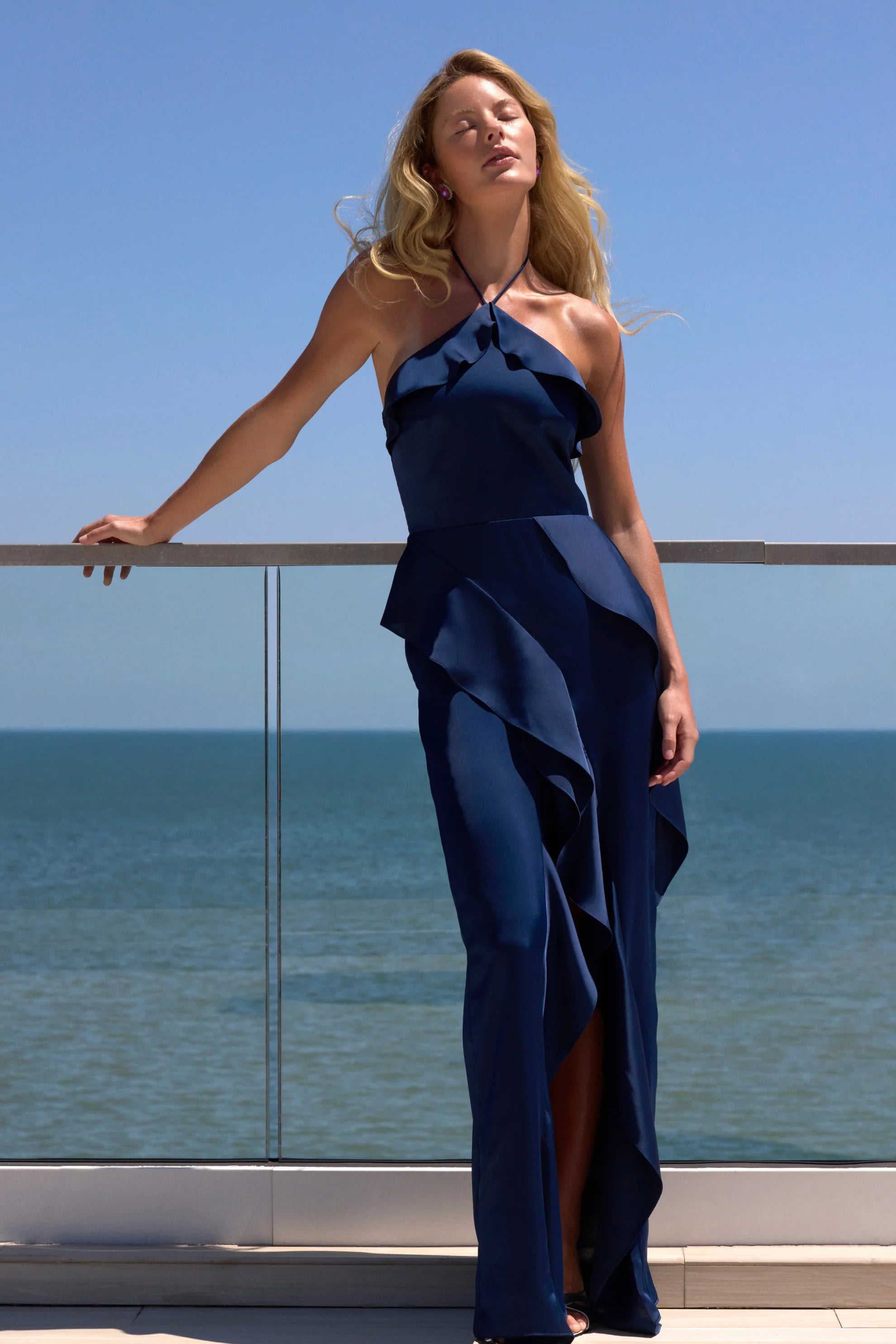 model wearing a dark blue ruffled dress by the ocean