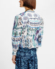 A model shown from the back wearing a white long-sleeve button-up shirt with a blue, purple, and green botanical pattern, paired with dark blue patterned trousers, against a plain white background.