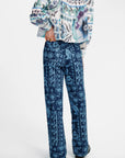 A model shown from the back wearing a patterned long-sleeve top and matching wide-leg trousers. The garments feature an intricate blue, white, and purple graphic print, photographed against a clean white studio background.
