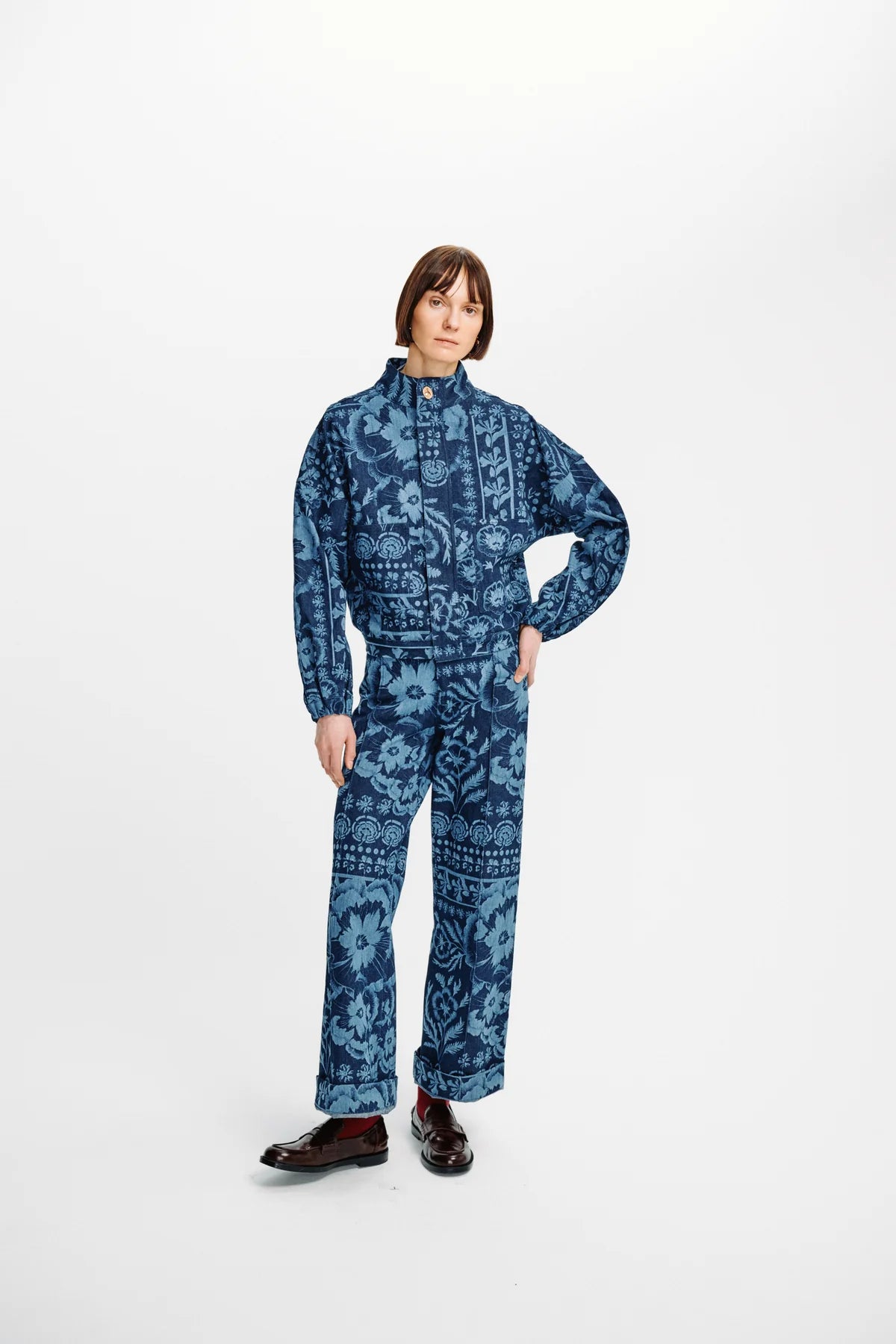 A model wearing a matching blue and navy patterned long-sleeve top and trousers set, styled with dark brown leather shoes, against a plain white studio background.