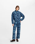 A model wearing a matching blue and navy patterned long-sleeve top and trousers set, styled with dark brown leather shoes, against a plain white studio background.