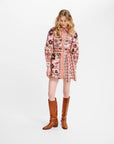 A woman modeling a long-sleeve mini dress with a pink and multicolor bohemian floral pattern, paired with brown knee-high boots, against a plain white studio background.