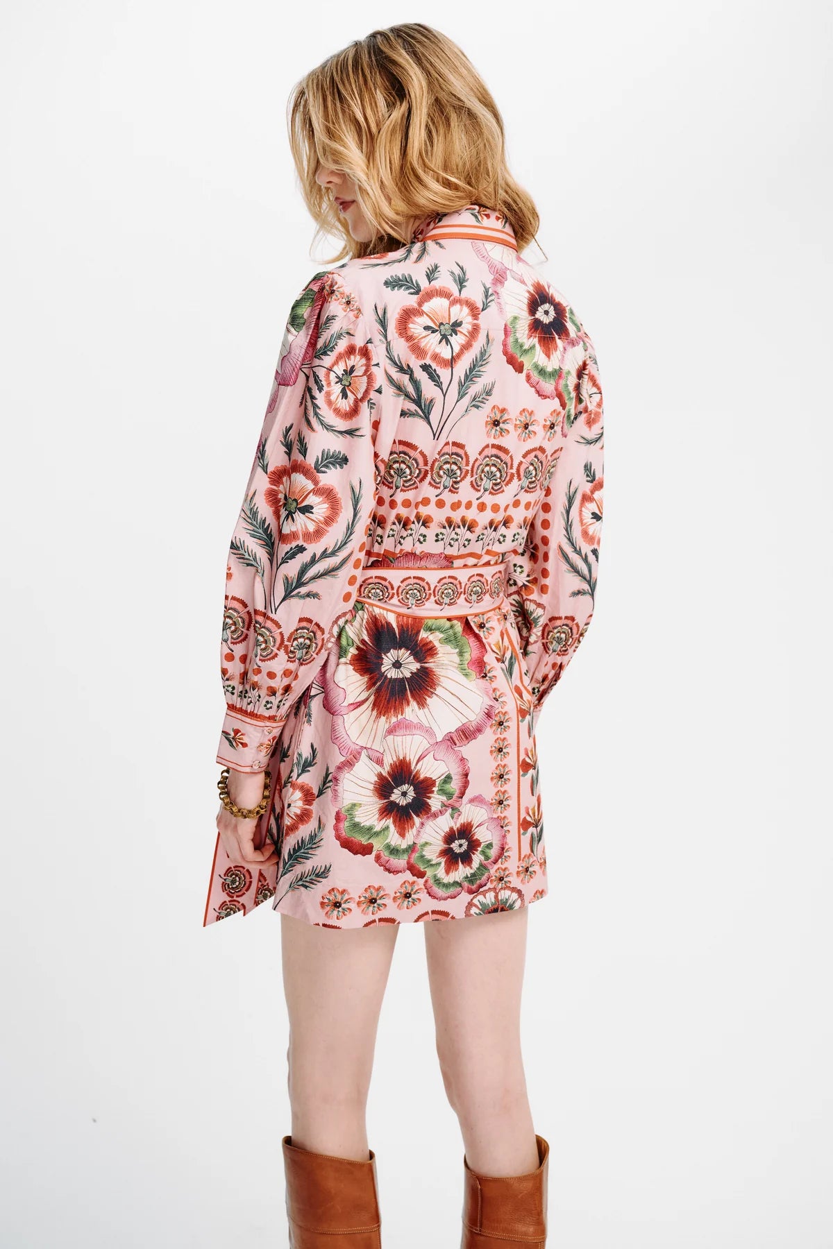 A woman shown from the back wearing a pink long-sleeve mini coat with a colorful floral and geometric pattern, paired with brown boots, against a plain white background.