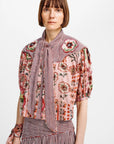 A model wearing a multi-patterned blouse with pink floral prints, red-and-white gingham, and puff sleeves, paired with a matching gingham skirt against a plain white background.