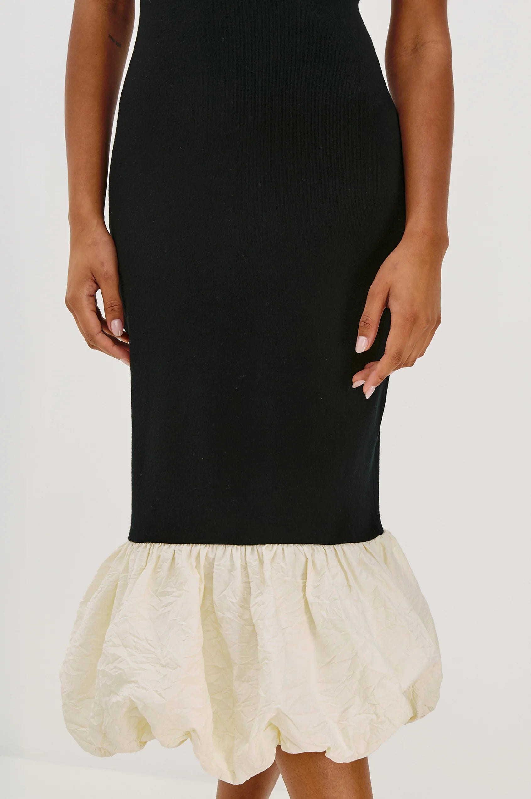 Black dress with a cream-colored ruffled bottom on a white background detail view