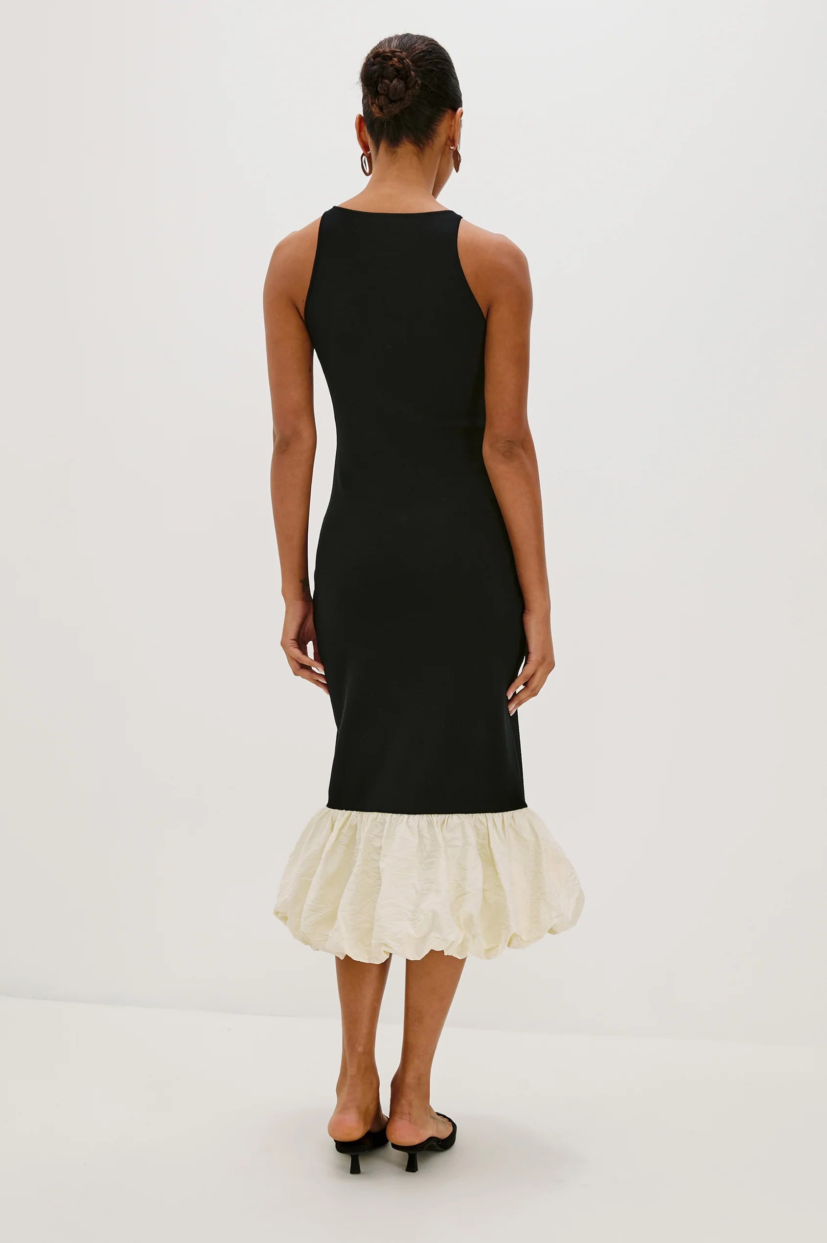 Black dress with a white ruffled hem on a white background back view