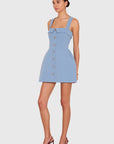 A model wearing a light blue sleeveless mini dress with a structured bodice, front buttons, and a flared skirt, paired with brown pointed-toe heels, set against a solid light gray background.