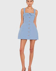 A model wearing a light blue sleeveless mini dress with a square neckline, button-front detail, and structured shoulders, paired with brown pointed-toe heels, against a light gray studio background.