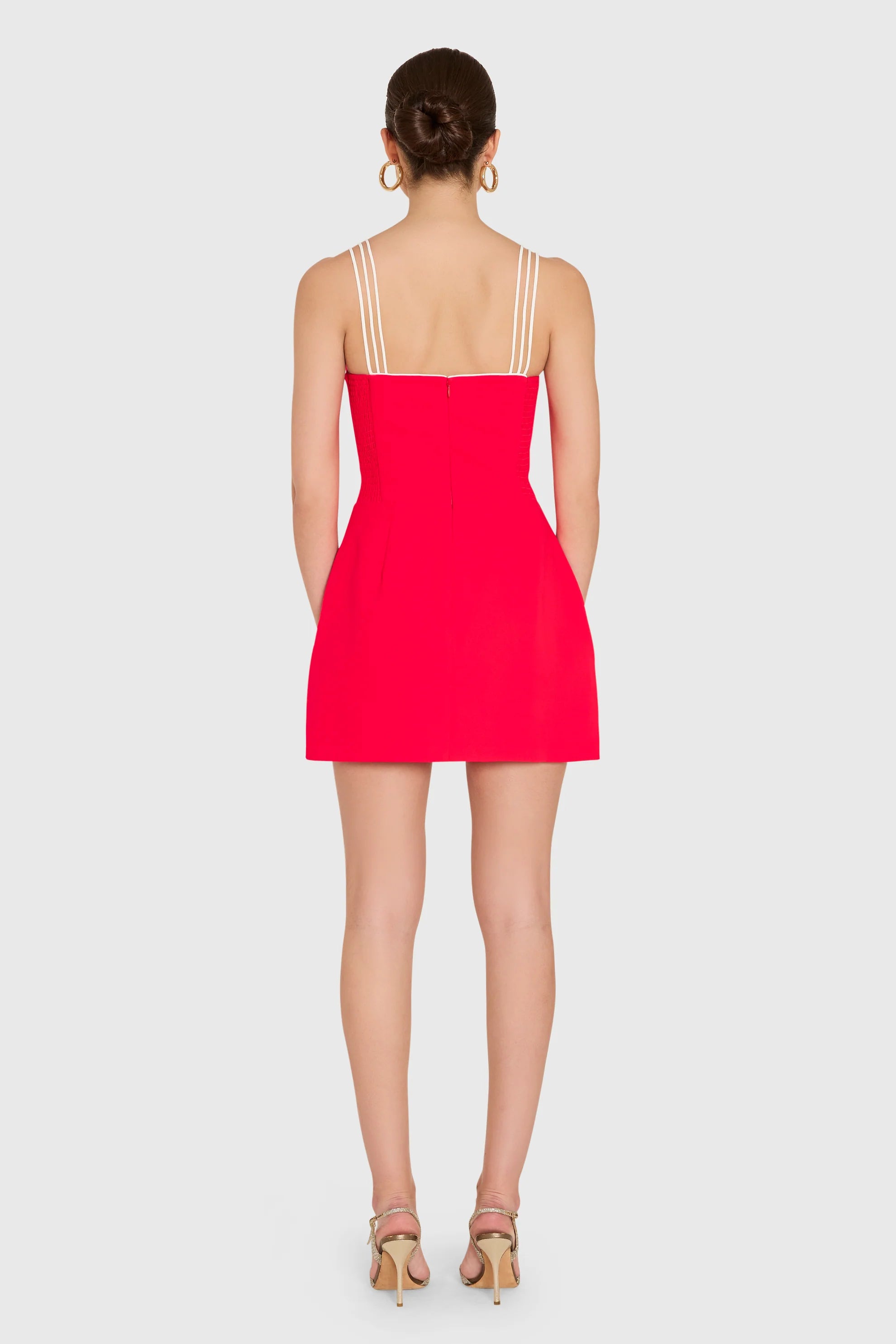 model wearing a red dress with ivory straps standing on a white background, back view