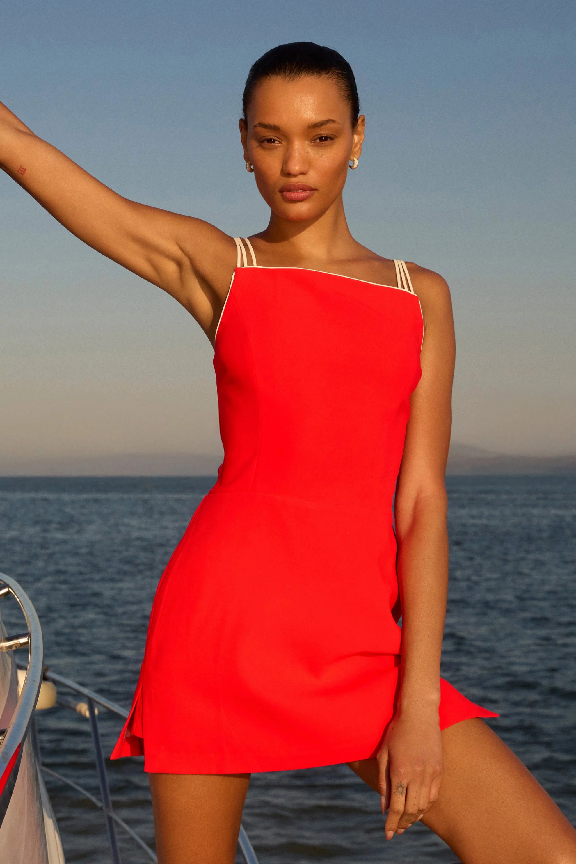 model wearing a red dress with ivory straps standing on a boat over the ocean