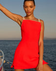 model wearing a red dress with ivory straps standing on a boat over the ocean