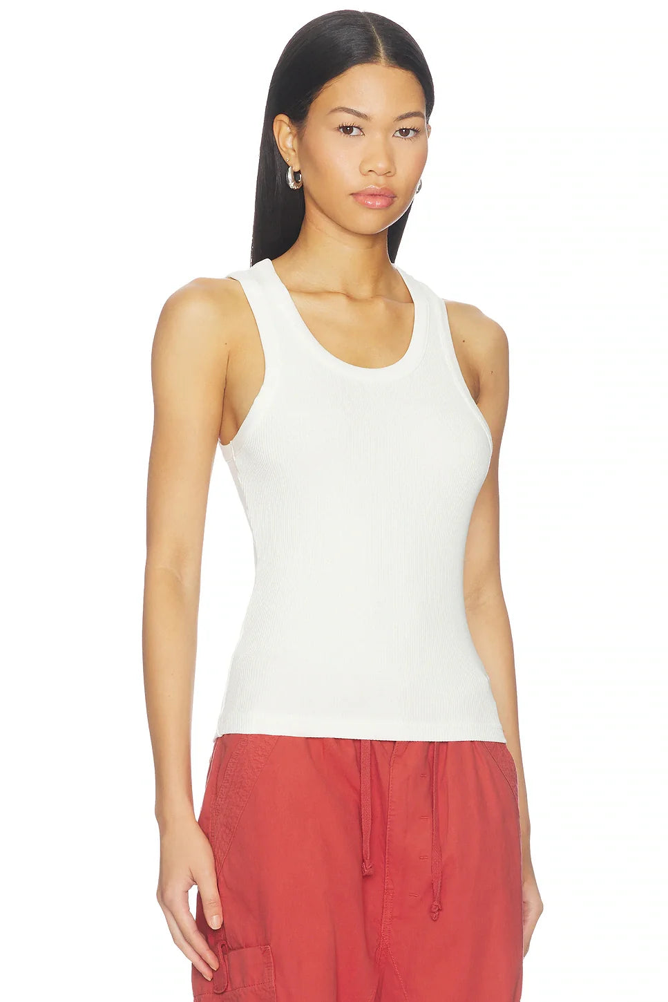 A woman modeling a white ribbed tank top paired with rust red drawstring pants against a plain white background.