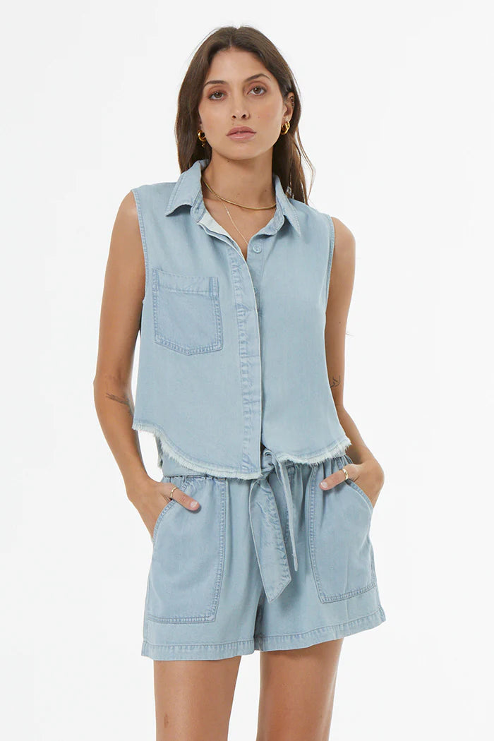 Woman wearing a light blue denim sleeveless shirt and shorts set on a white background