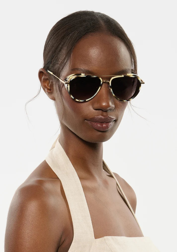 Woman wearing gold-framed sunglasses against a plain background
