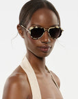 Woman wearing gold-framed sunglasses against a plain background