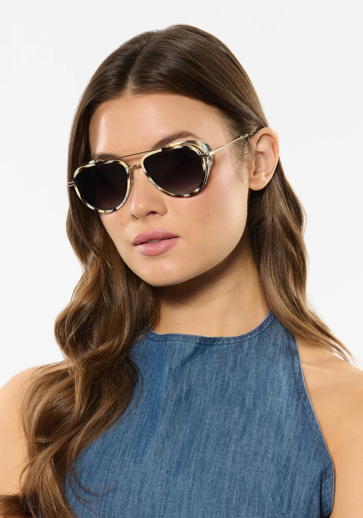 Woman wearing gold-framed sunglasses with a plain background