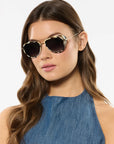 Woman wearing gold-framed sunglasses with a plain background