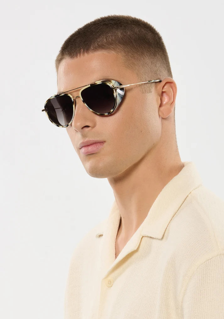 Man wearing aviator sunglasses and a light-colored shirt against a plain background