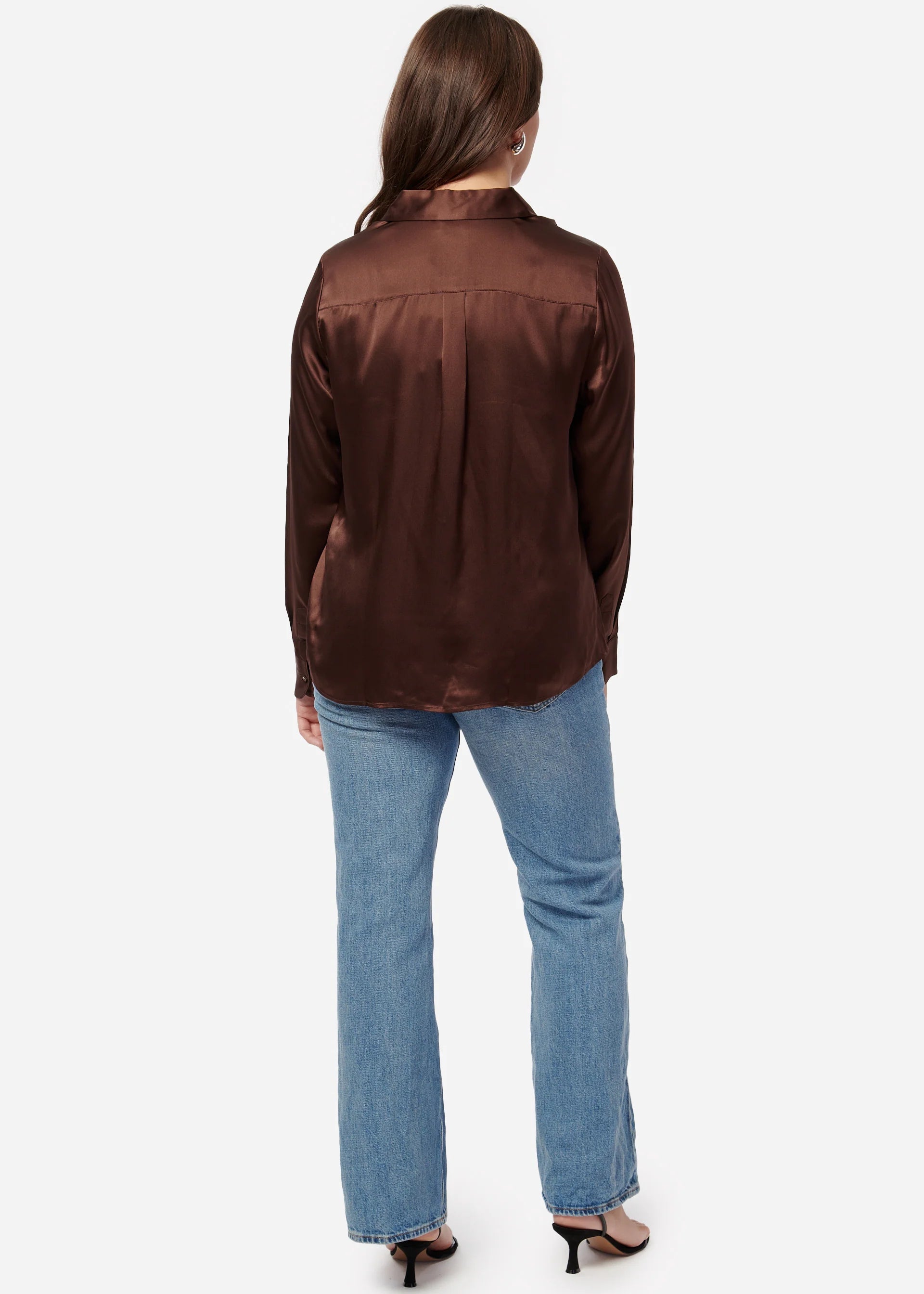 Person wearing a brown satin shirt and blue jeans on a white background