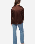 Person wearing a brown satin shirt and blue jeans on a white background