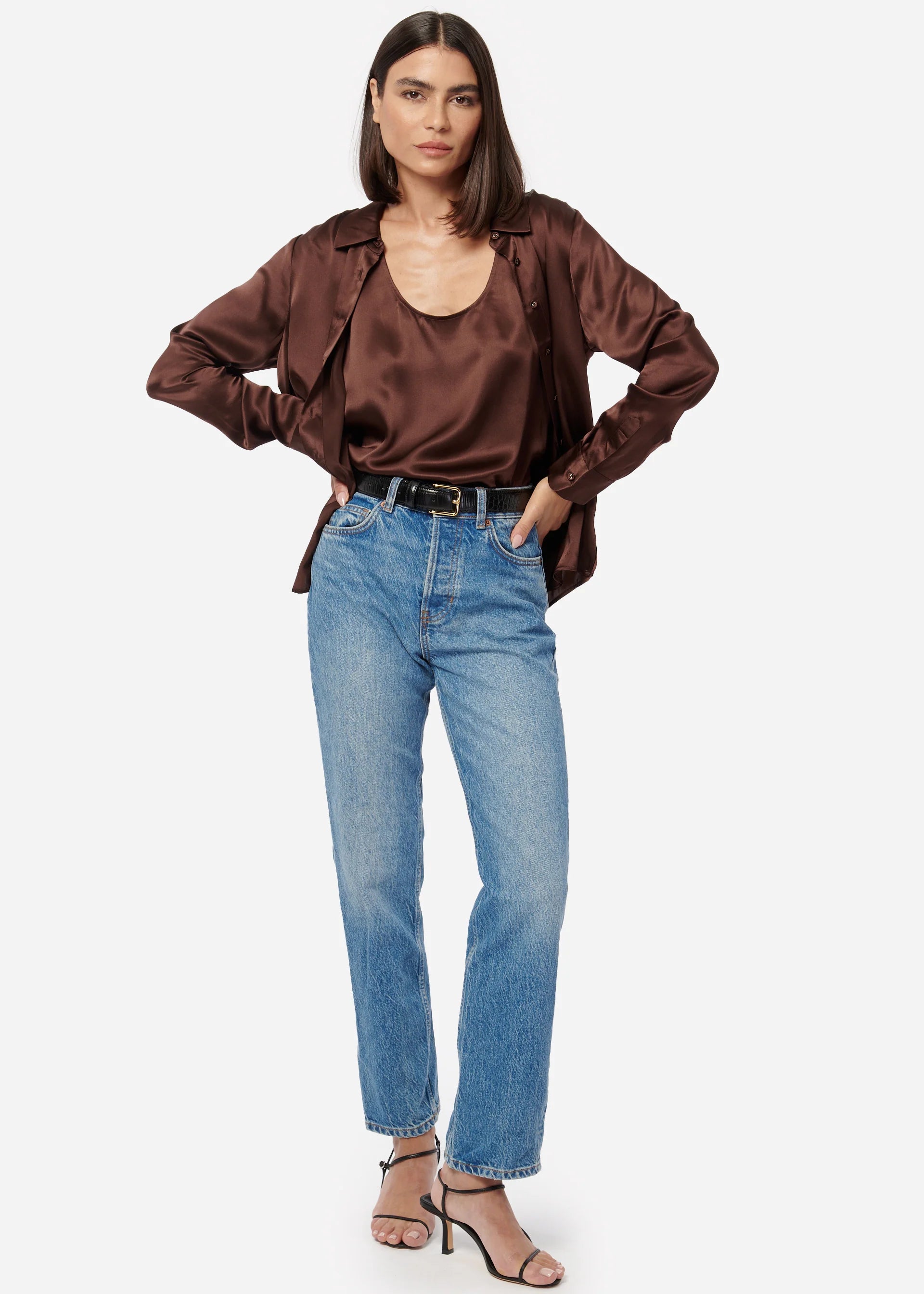Woman wearing a brown satin blouse and blue jeans on a white background