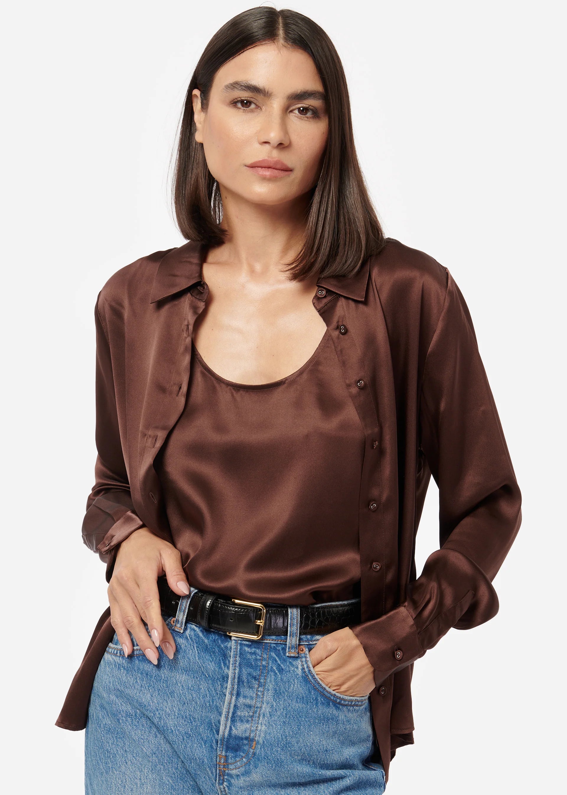 Woman wearing a brown satin shirt over a beige top with blue jeans on a white background