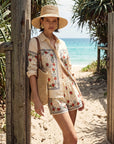 Woman in a floral set and straw hat standing on a sandy path with ocean view