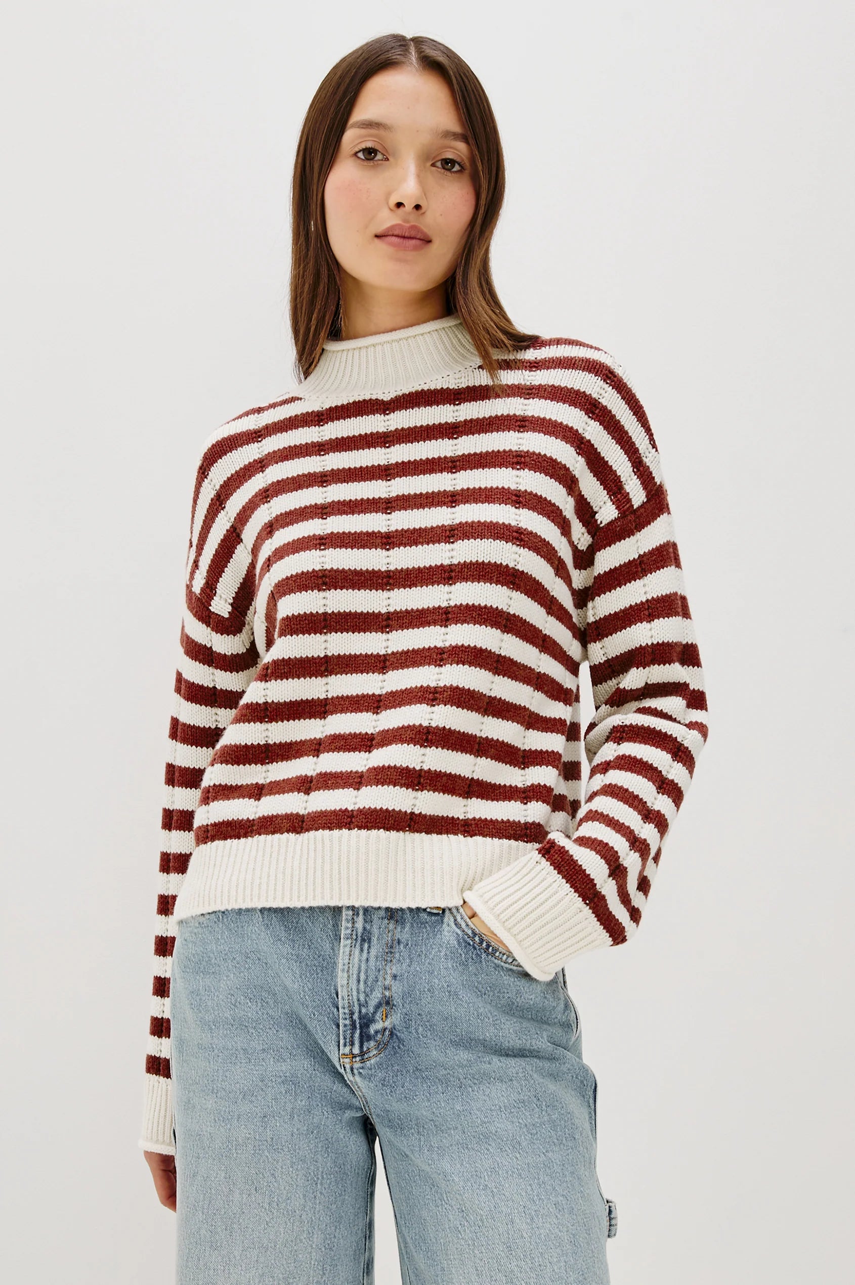 Person wearing a red and white striped sweater with light blue jeans on a plain background
