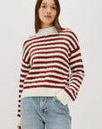 Person wearing a red and white striped sweater with light blue jeans on a plain background