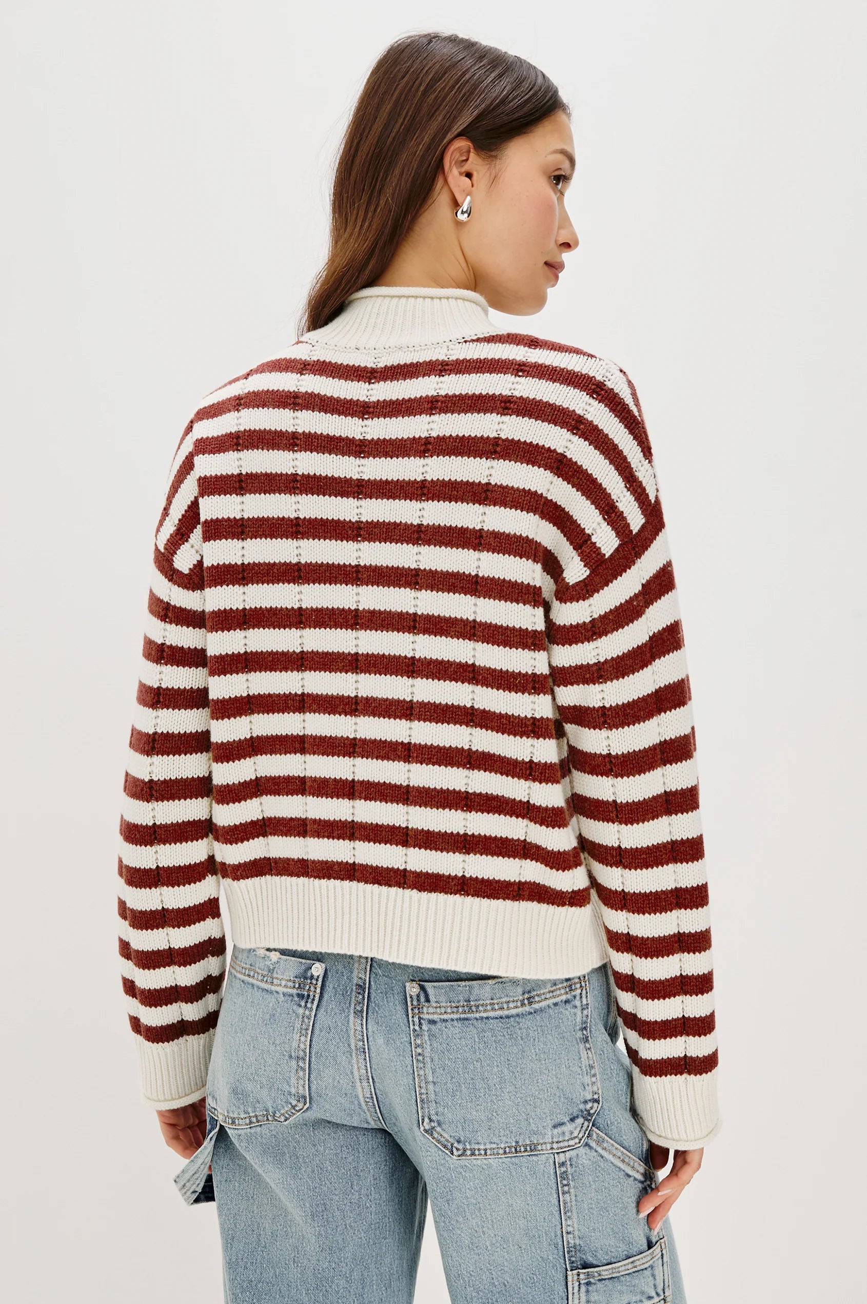 Person wearing a red and white striped sweater with light blue jeans on a plain background, back