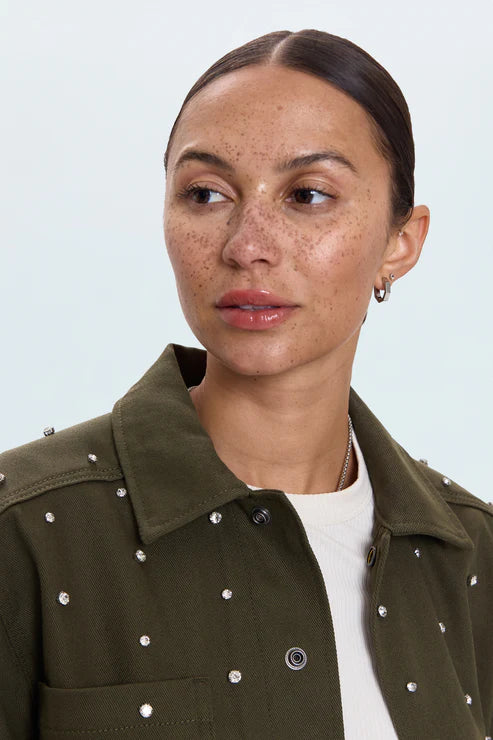 Woman wearing a green jacket with white embellishments on a light gray background