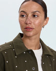 Woman wearing a green jacket with white embellishments on a light gray background
