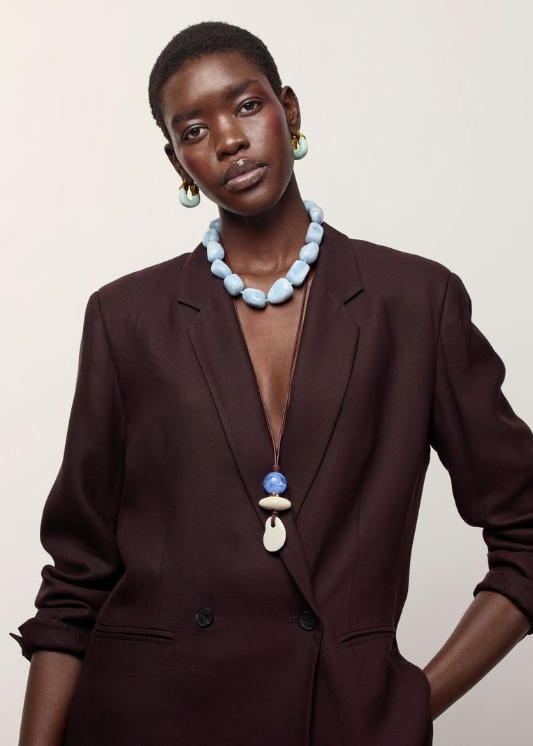 A model wearing a dark brown blazer, Sea and Sky Collar and Museo Cord II Necklace in Sea, posed against a solid off-white background.