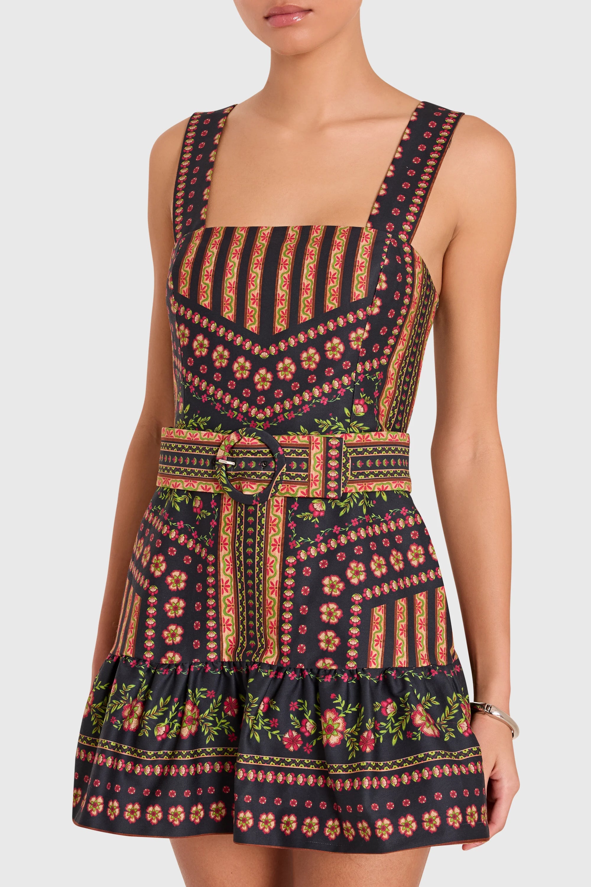 A sleeveless mini dress with a square neckline and wide shoulder straps, featuring a dark navy base with a colorful geometric and floral pattern in red, orange, green, and yellow. The dress includes a matching waist belt with a ring detail and is shown on a model against a light gray background.