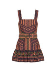 A sleeveless mini dress with a wide shoulder strap, featuring a geometric and floral bohemian pattern in orange, red, green, and black. It includes a matching fabric belt with a decorative metal buckle at the waist.