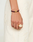 Hand wearing a gold ring and purple bracelet on a white background