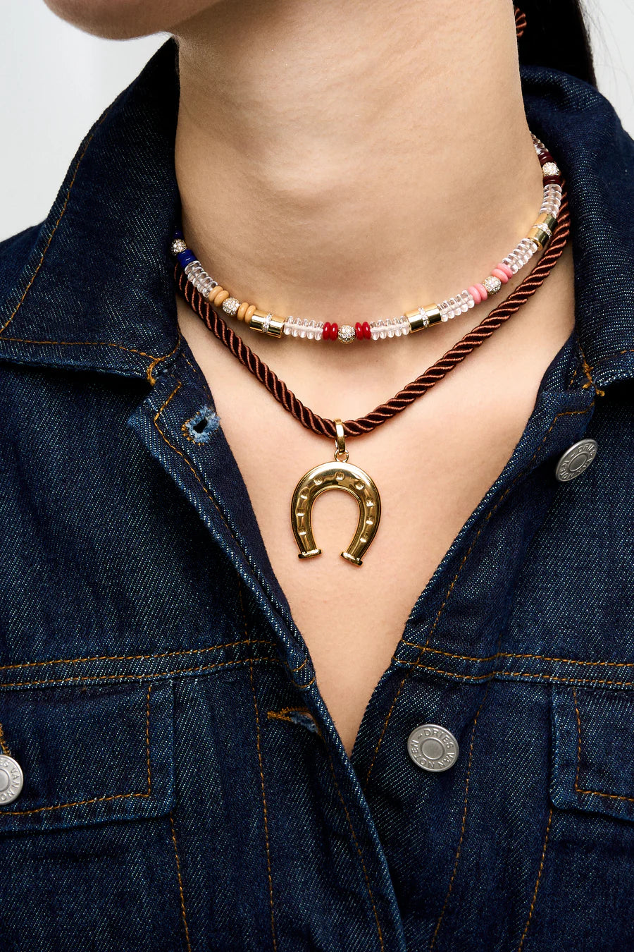 Necklace with a horseshoe pendant worn by a person in a denim jacket.