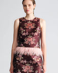 A sleeveless dark burgundy mini dress with a pink floral jacquard pattern and a light pink feather trim at the waist, modeled against a light gray background.