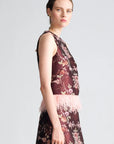 A woman modeling a sleeveless dark floral dress with a light pink feathered waistband, shown in profile against a light gray studio background.