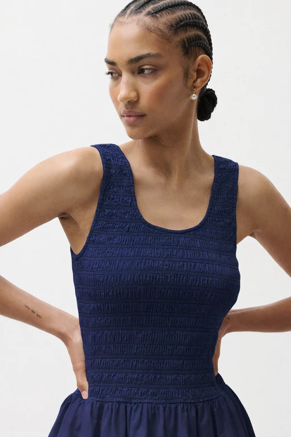 Woman wearing a blue sleeveless dress against a plain background