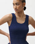 Woman wearing a blue sleeveless dress against a plain background