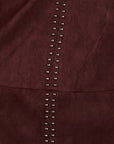 Close-up of a dark burgundy suede or faux-suede material with a vertical row of metallic silver studs down the center.