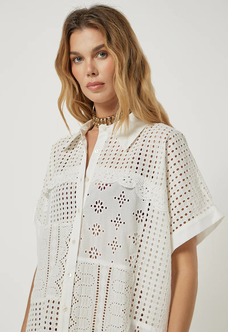 Woman wearing a white crochet top against a plain background